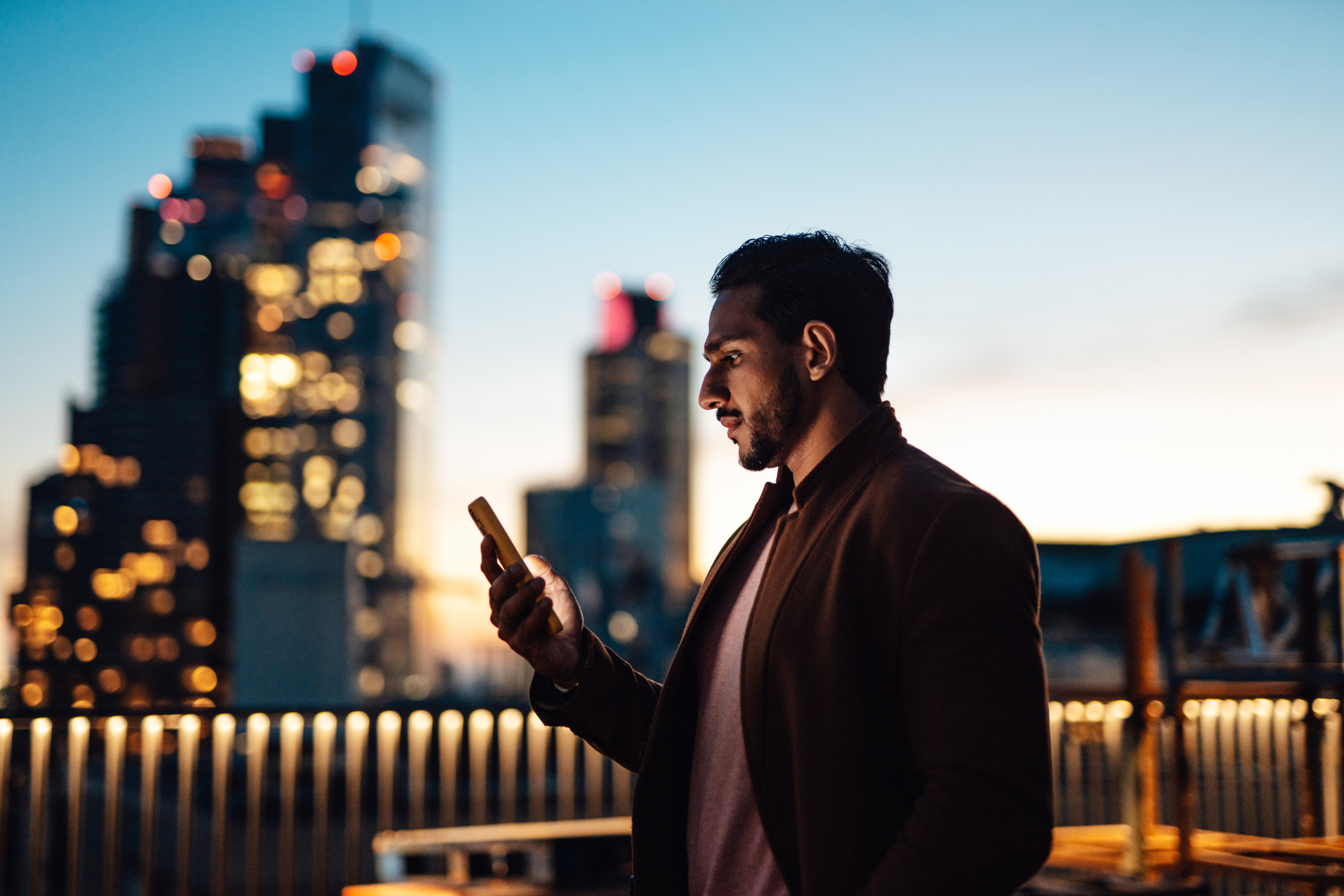 Telus - Businessman using mobile phone at rooftop in business building against illuminated financial buildings and London cityscape at night